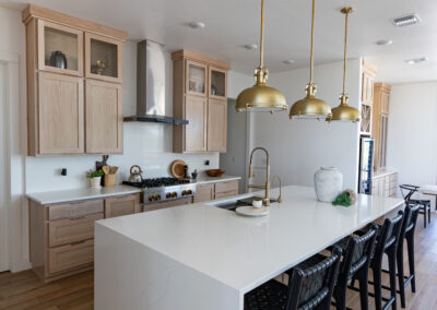 Luxurious kitchen in Austin, TX featuring Maestro Quartz Calacatta Rafael countertops, natural wooden cabinets, and elegant brass pendant lights