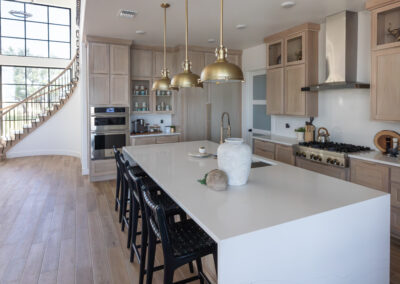 Luxurious kitchen in Austin, TX featuring Maestro Quartz Calacatta Rafael countertops, natural wooden cabinets, and elegant brass pendant lights