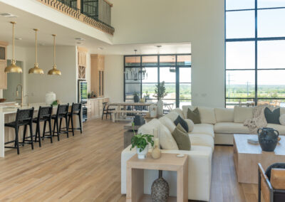 Modern kitchen and living space in Austin, TX featuring Maestro Quartz Calacatta Rafael countertops, natural wooden cabinets, and stylish brass pendant lights